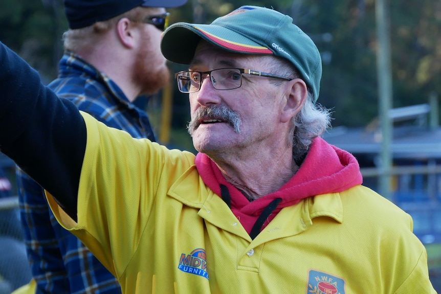 A football volunteer pointing towards a player, wearing a cap. 