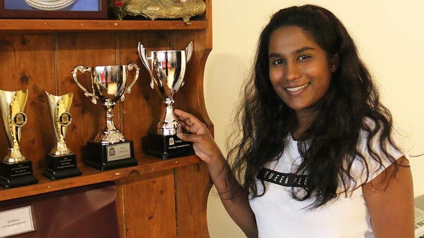 Soumiga Gopalakrishnan smiles as she stands beside some of the awards she had achieved at school.