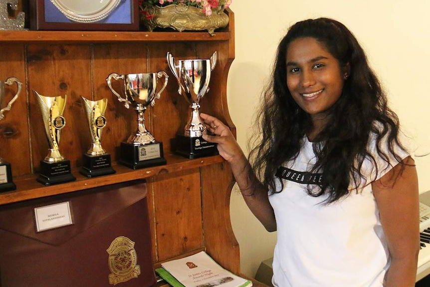 Soumiga Gopalakrishnan smiles as she stands beside some of the awards she had achieved at school.