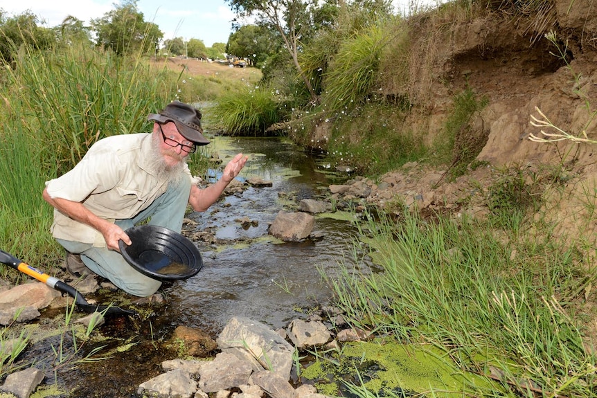 A man crouching next to a creek holding a fossicking pan