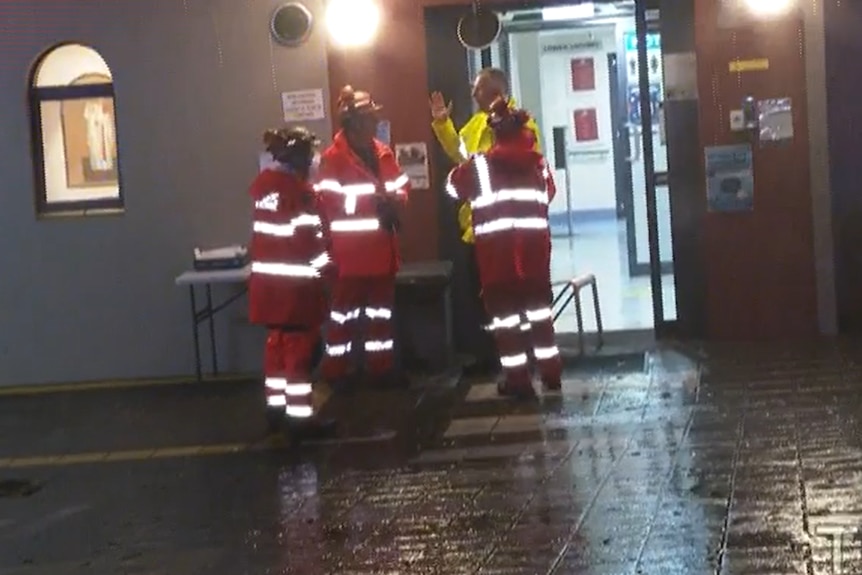 Four people in fluoro clothes stand in the rain outside a building