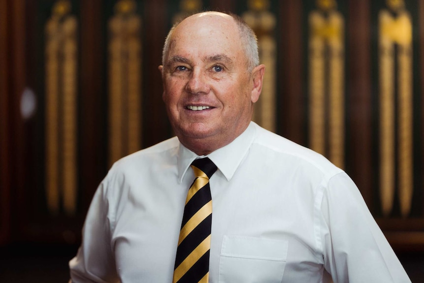 A head and shoulders picture of a balding man wearing a white shirt and yellow striped tie.