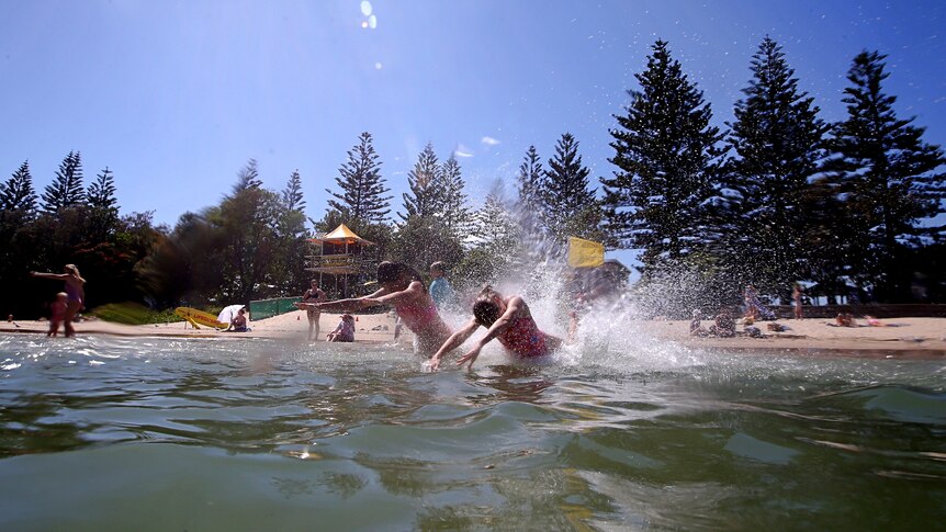 children dive into the ater at the beach, it's a sunny day and a lifeguard tower can be seen in the background