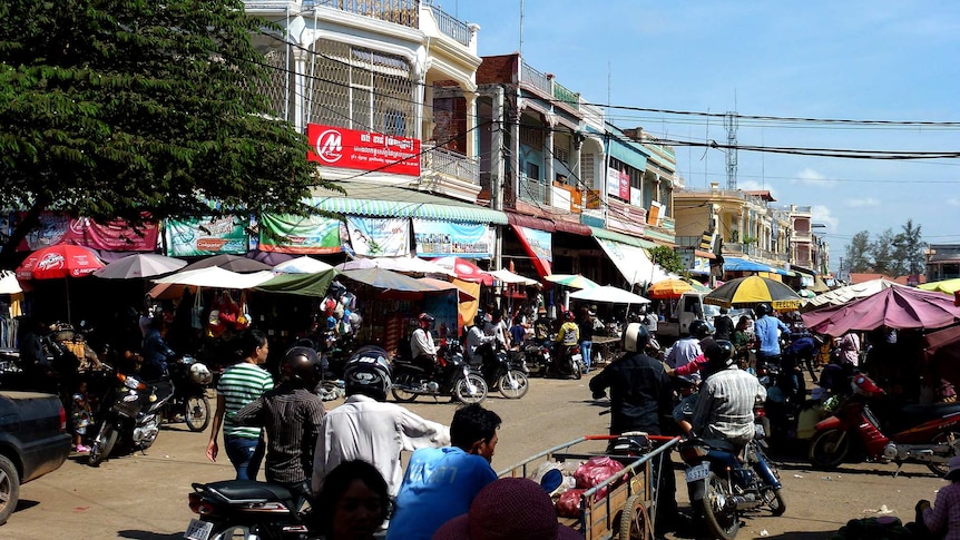 A busy street and market in Cambodia with dozens of people on motorcycles.