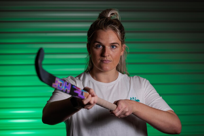 A serious looking woman points a hockey stick towards the camera. 