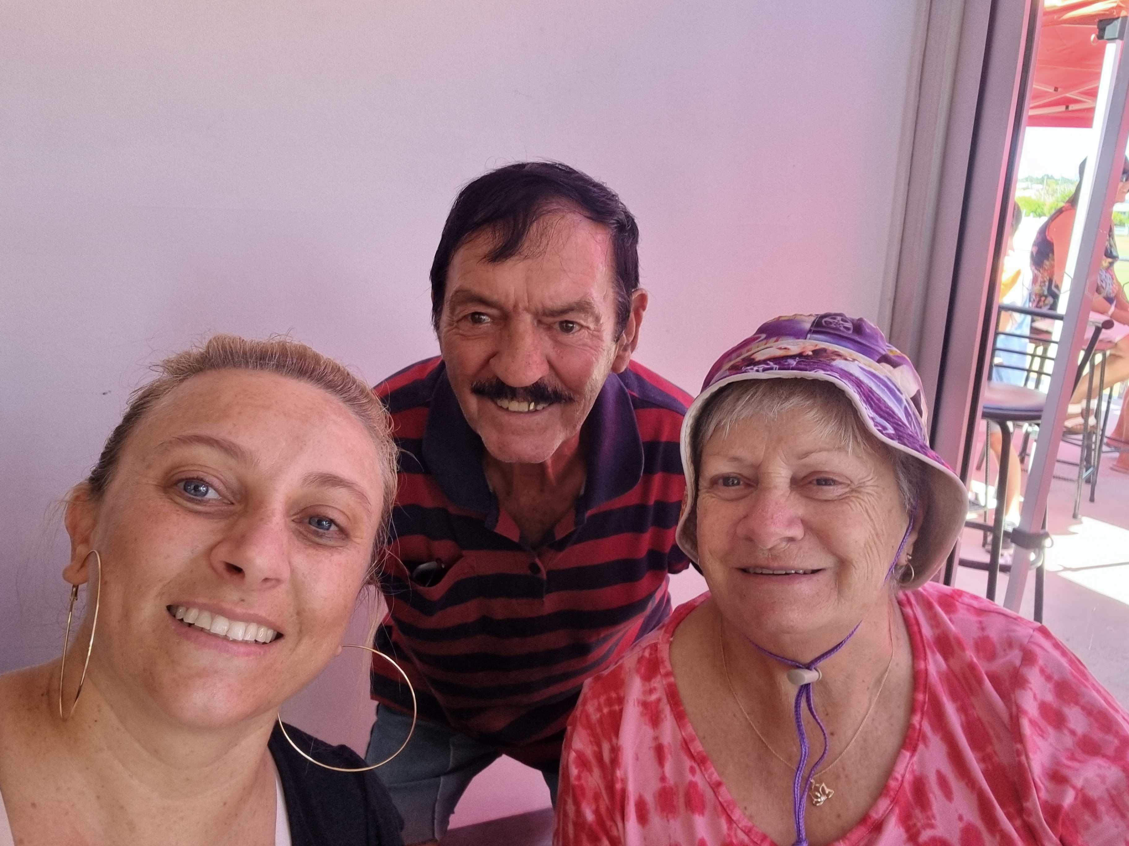 A selfie with a middle-aged woman and her older parents against a pink background