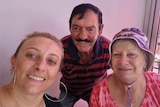 A selfie with a middle-aged woman and her older parents against a pink background