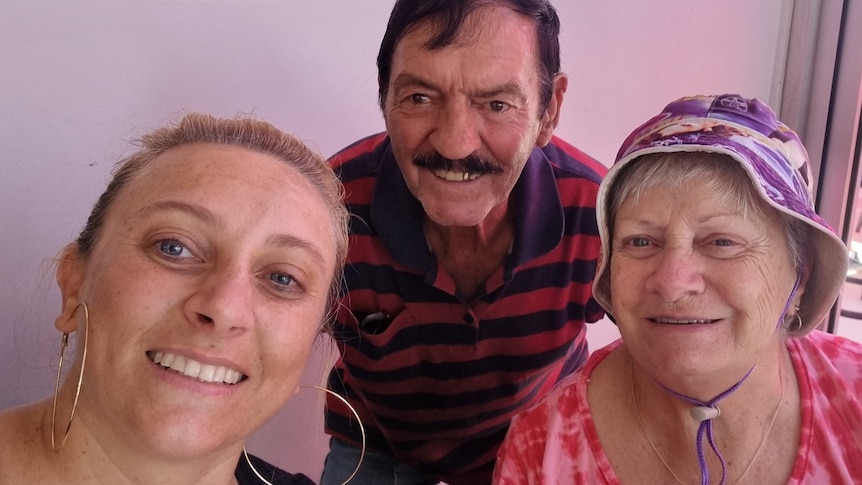 A selfie with a middle-aged woman and her older parents against a pink background