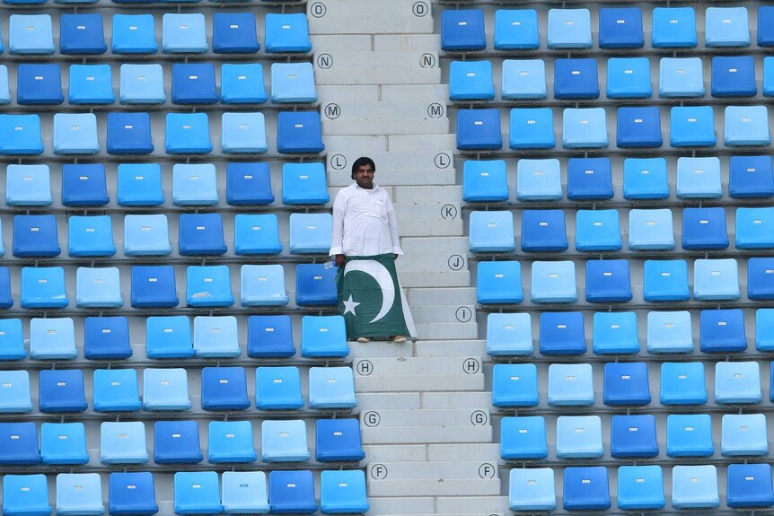 Telephoto shot of a solitary man standing in a grandstand holding a Pakistan flag.
