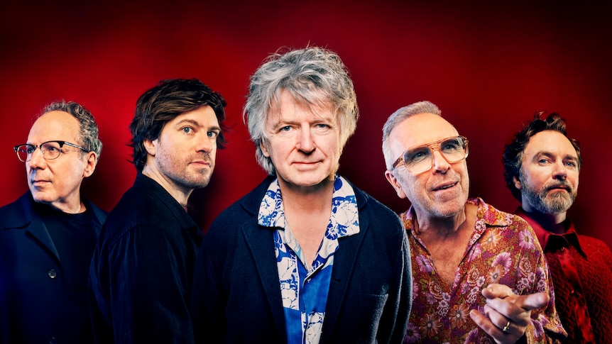 Five members of band Crowded House before a dark red background