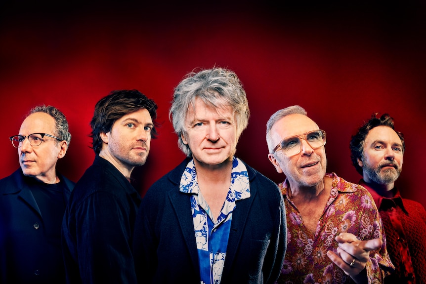 Five members of band Crowded House before a dark red background