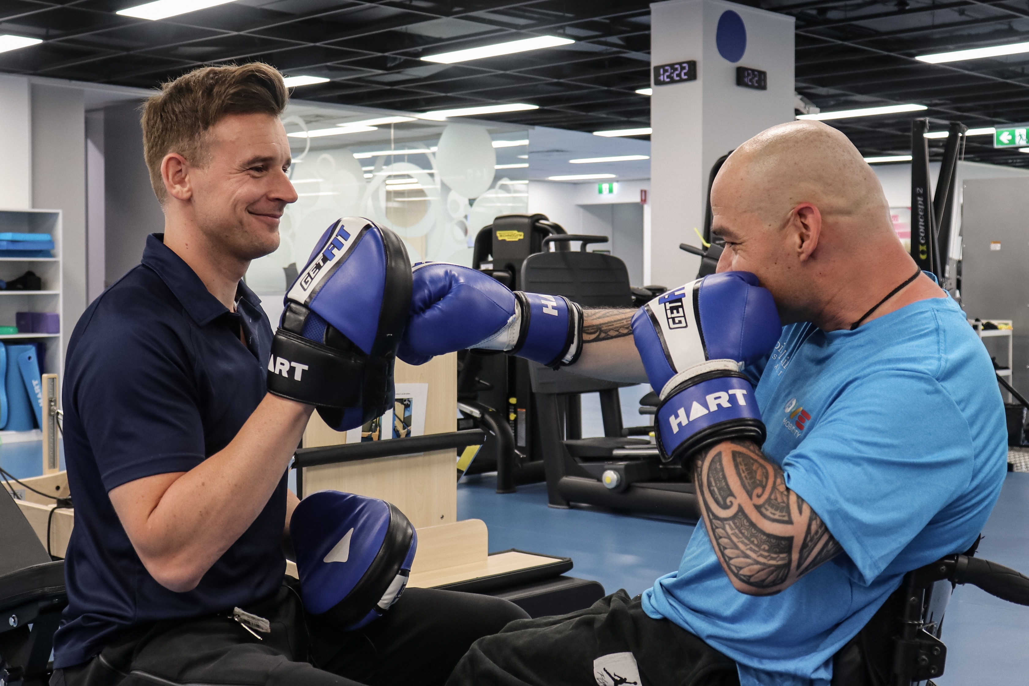 A man with tattoos punching a man holding boxing gloves.