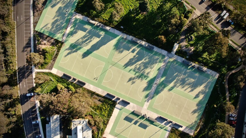 Aerial view of eight netball courts surrounded by trees and a car park on left