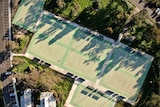 Aerial view of eight netball courts surrounded by trees and a car park on left
