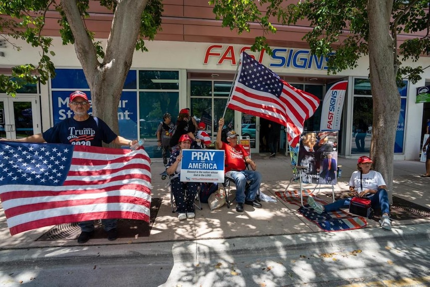 A group of people with US flags sitting on a sidewalk