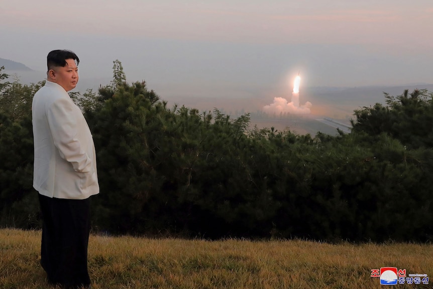 A man in white clothes with a missile launching in the background 