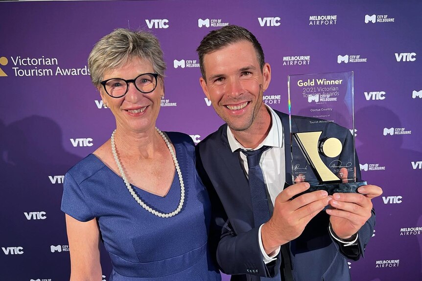 A man holds up an award while standing next to a woman in front of a purple background