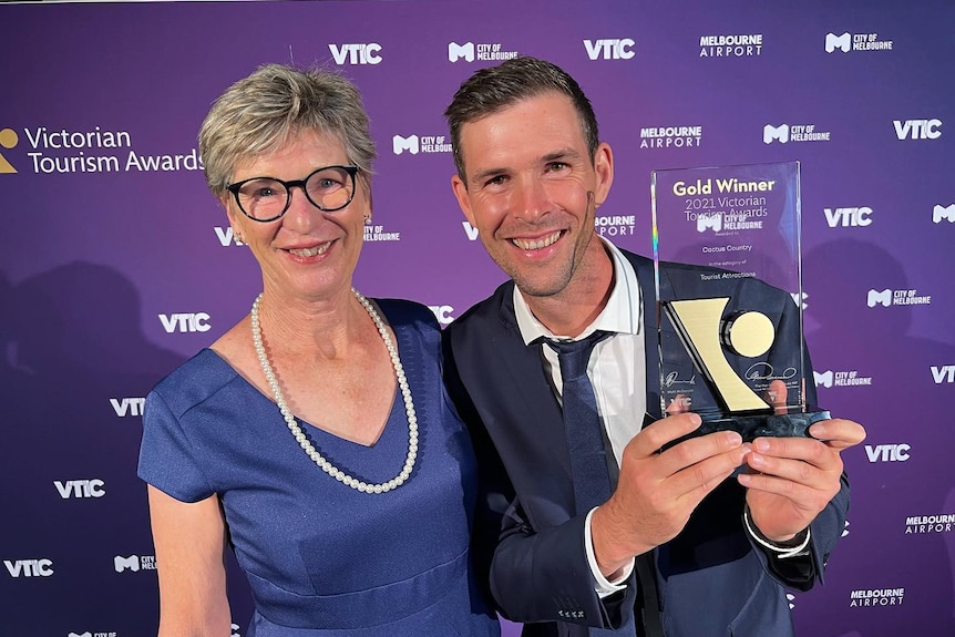 A man holds up an award while standing next to a woman in front of a purple background