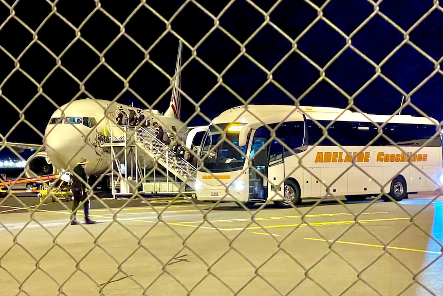 Through fencing, people can be seen climbing stairs to get into a plane.