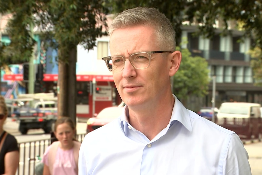 a man wearing glasses standing outdoors talking to the media