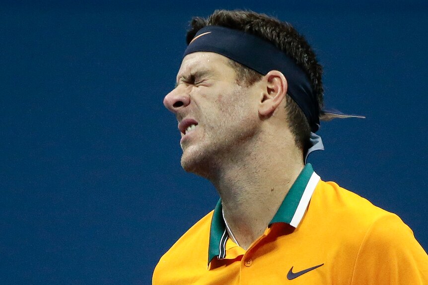 A male tennis plyer wearing yellow grimaces.