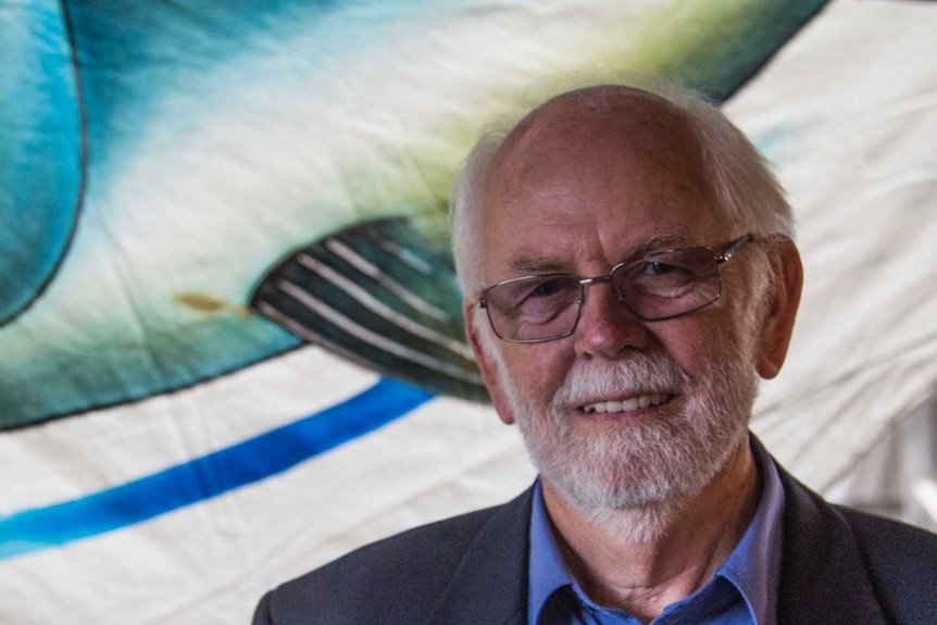 Documentary director Garry Kerr stands in front of a large, colourful banner of a cartoon tuna fish.
