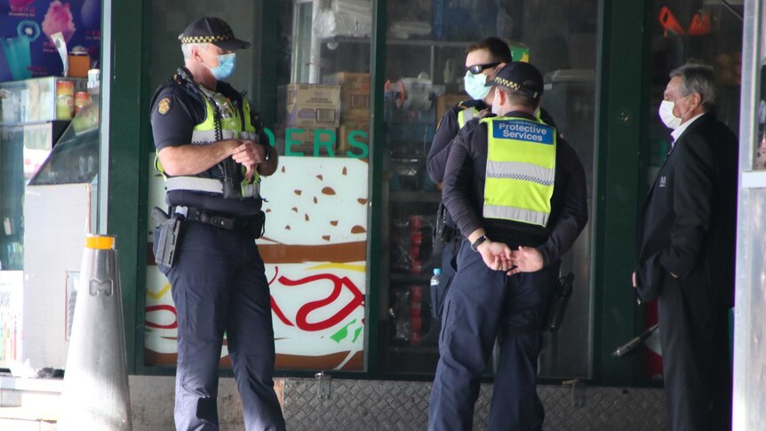Three Victoria Police officers wearing masks stand outside a store.