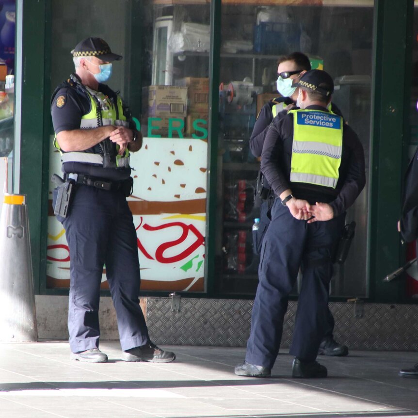 Three Victoria Police officers wearing masks stand outside a store.