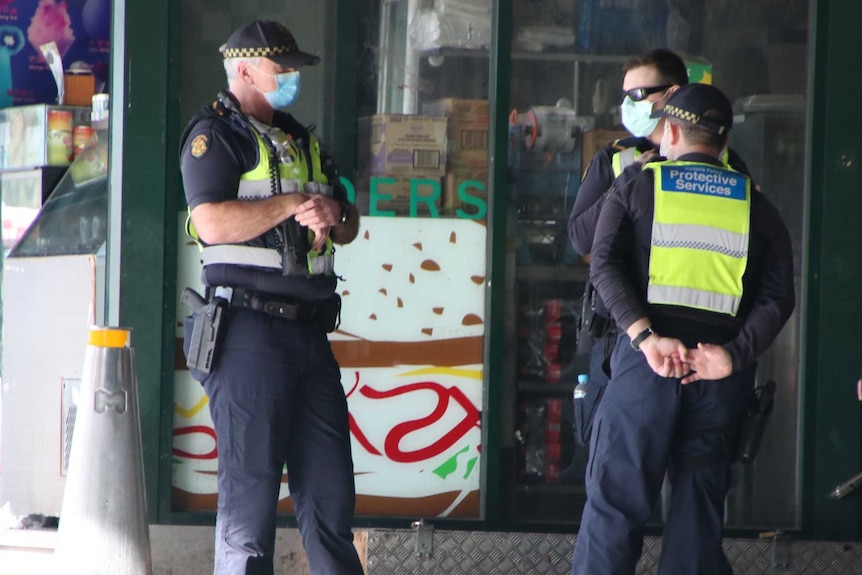 Three Victoria Police officers wearing masks stand outside a store.