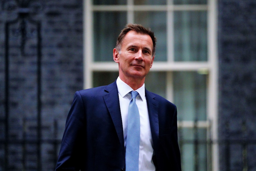 A man in suit walking with a window behind him. 