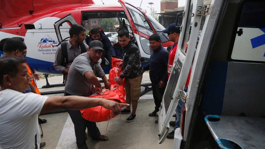 People carry an orange body bag from a helicopter into an ambulance.