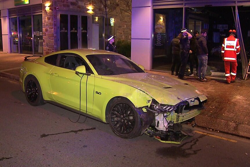 A green Mustang all smashed at the front after it hit a shop