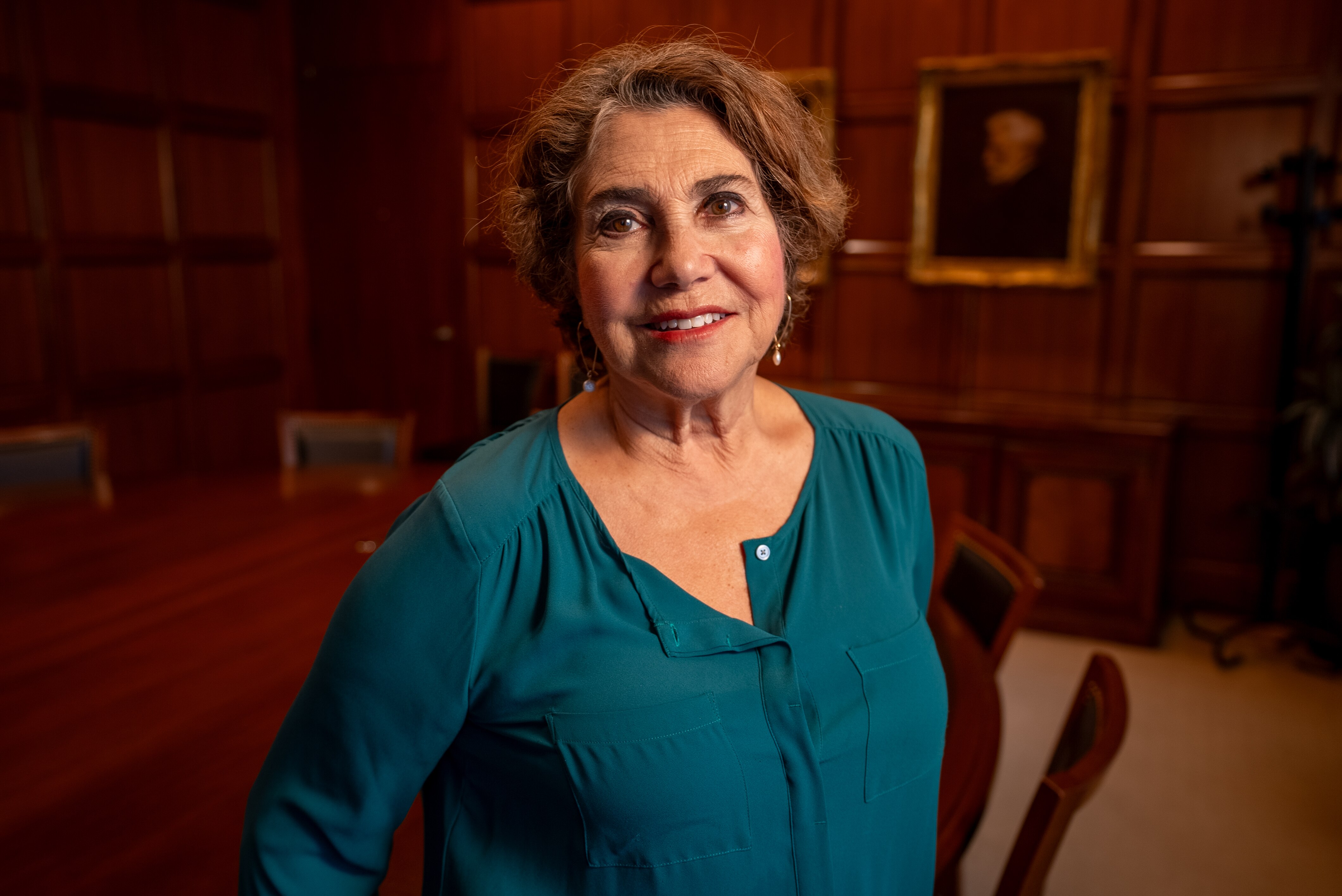 Middle-aged woman in a teal blouse sitting in a boardroom.