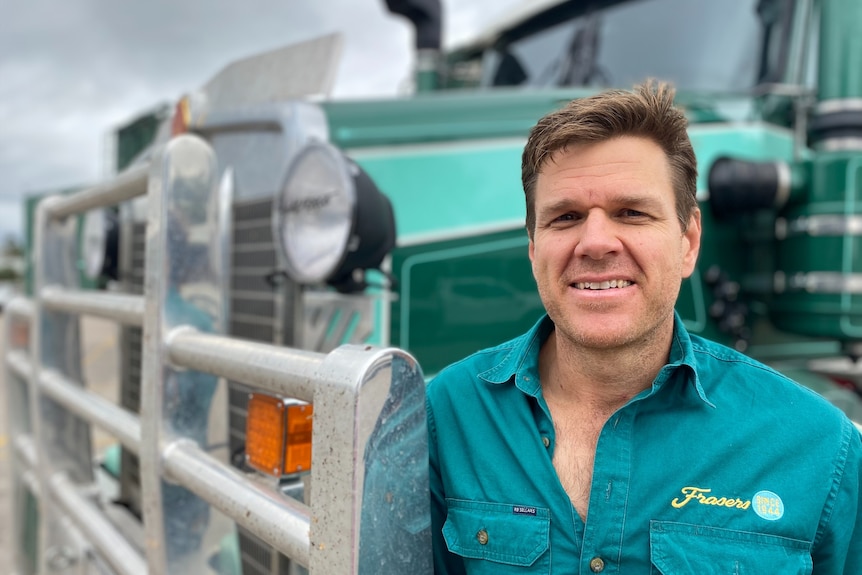 A man in a green shirt standing in front of a large green truck