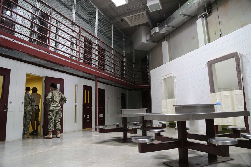 The cell block inside Camp 6, with a common area with metal tables and attached seats, next to cells with numbered doors