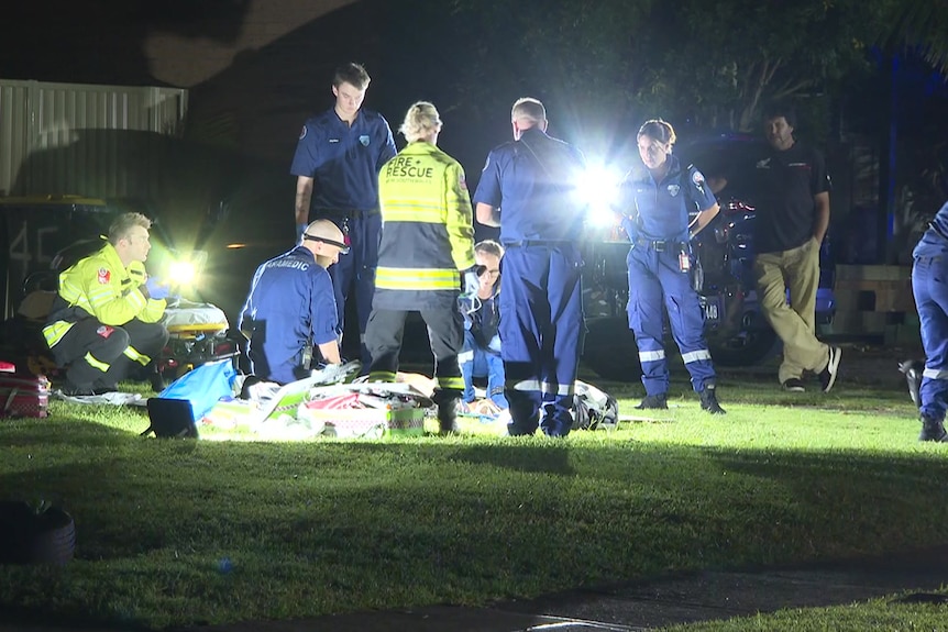 Emergency workers help a man lying on the ground at night time.