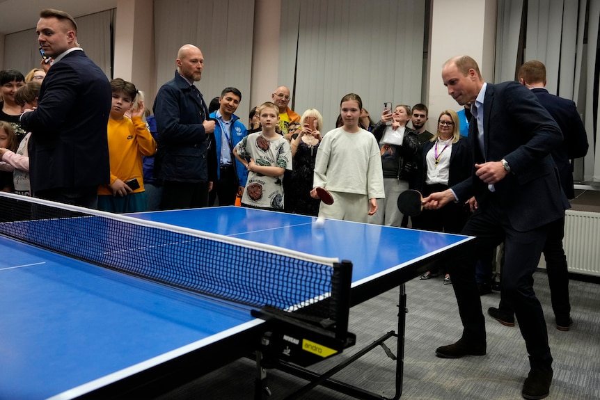 Prince William leans to the left as he prepares to hit a ping pong ball with his racquet