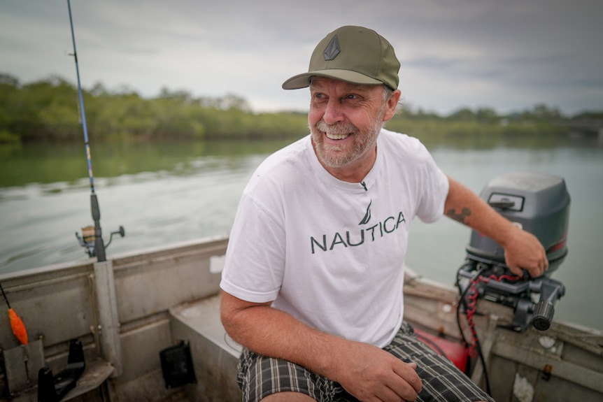 Brett laughs as he steers a small fishing boat, with a rod wedged into the side.