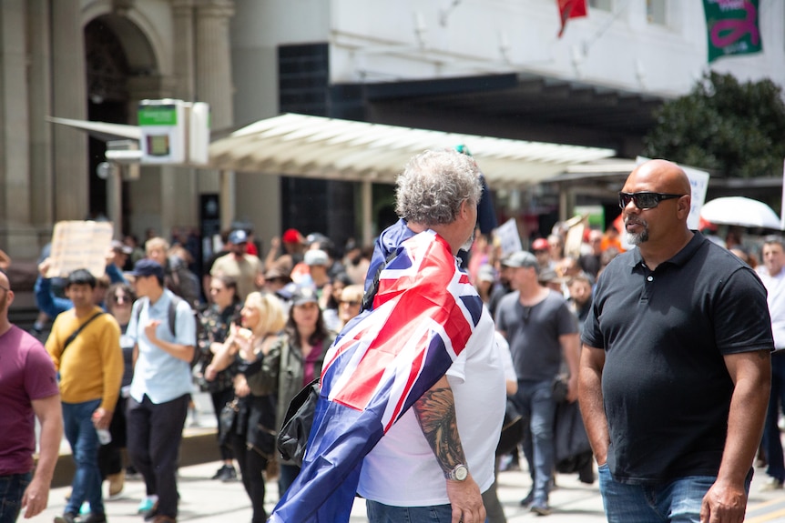 A person wearing a white tshirt with an Australian flag on top surrounded by a crowd in Melbourne.
