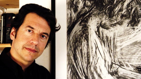 You view a younger George Monbiot posing next to a charcoal artwork. 