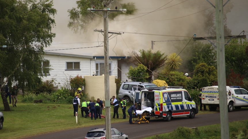 Police gather around a man on the ground as smoke rises from a house