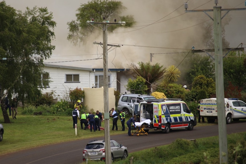Police gather around a man on the ground as smoke rises from a house