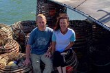 A man and woman are sitting in a boat with lobster cages all around them