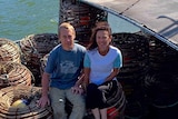A man and woman are sitting in a boat with lobster cages all around them