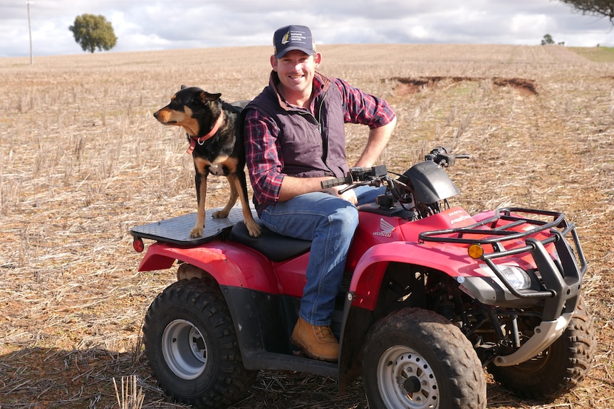 A young man sitting on a red quadbike with a dog