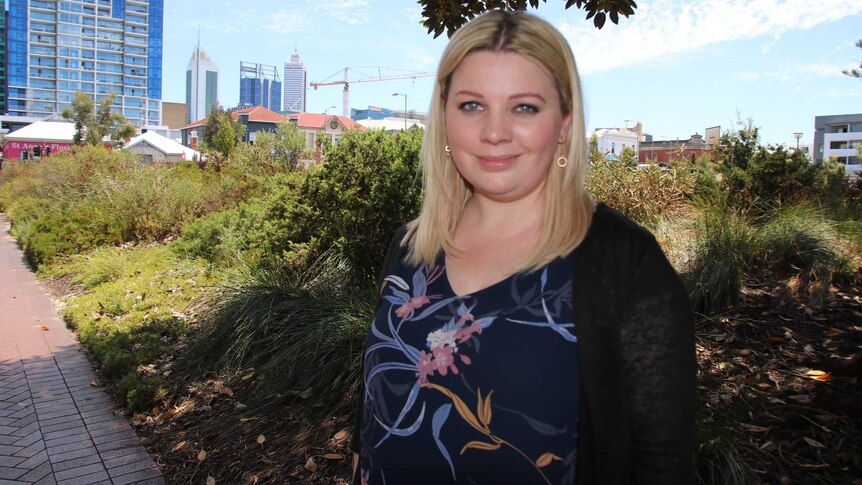 Perth woman Nikki Atack standing on a footpath in the city with shrubs and buildings in the background