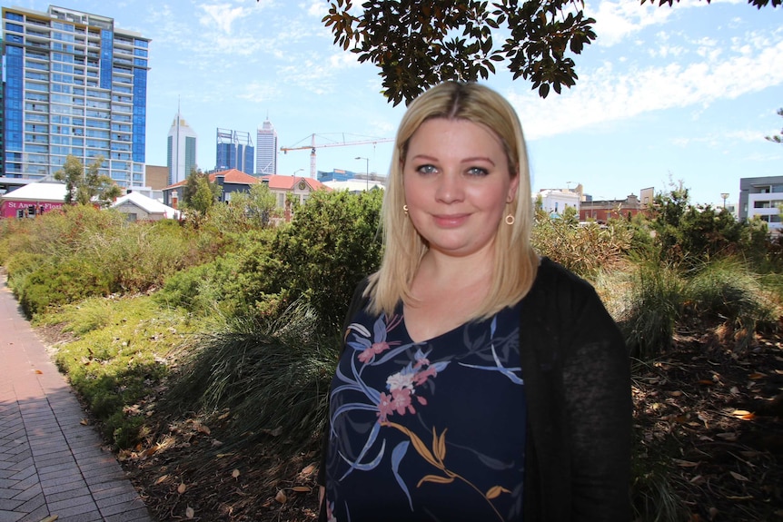 Perth woman Nikki Atack standing on a footpath in the city with shrubs and buildings in the background