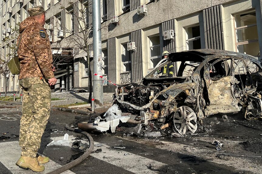 Soldiers stand next to a car destroyed by shelling. 