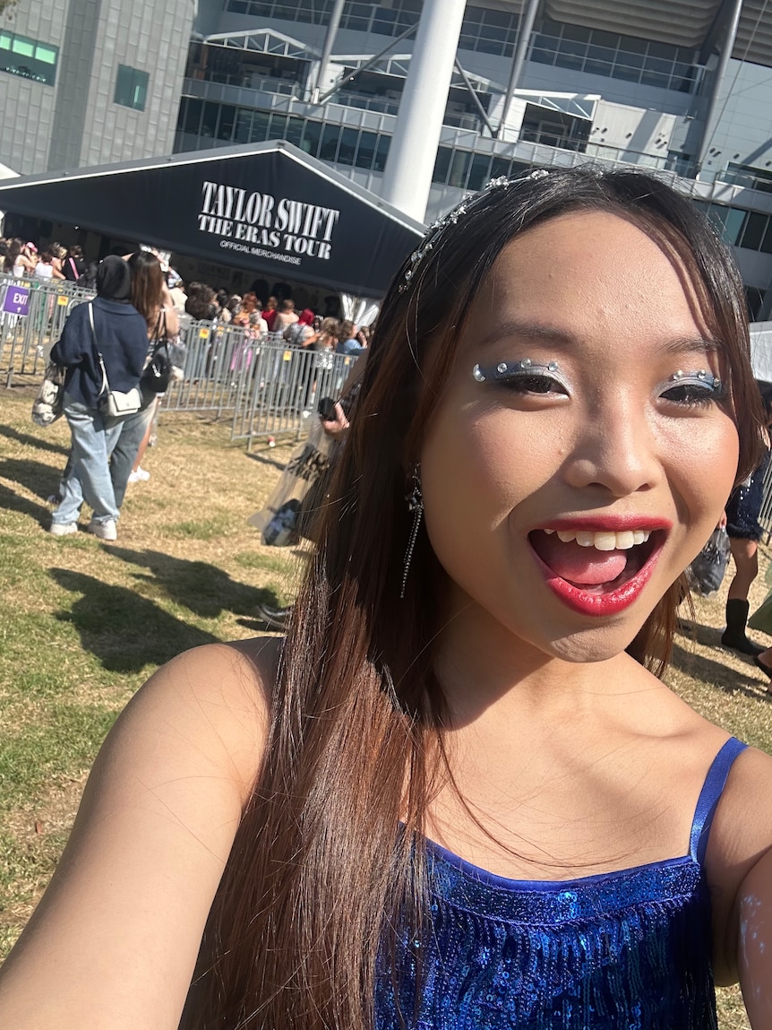 Asian woman standing outside stadium to Taylor Swift concert. 
