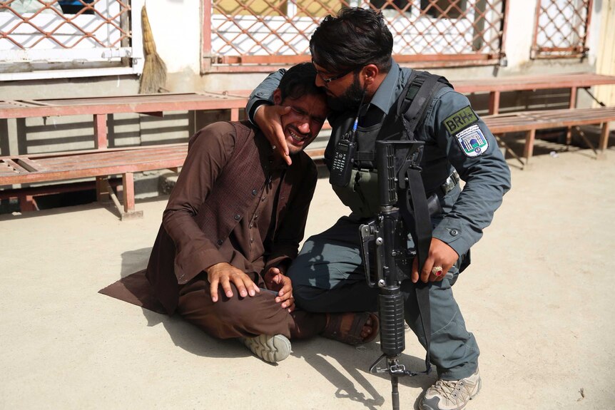 Afghan policeman comforts a man crying on the ground.